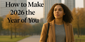 A young woman with curly hair in a tan coat walks in a park with autumn trees and tall buildings. Text reads, How to Make 2026 the Year of You.