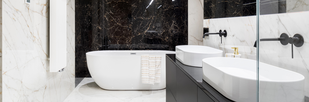 Modern bathroom with white marble walls and floor, a freestanding white bath with a towel draped over the edge, black marble feature wall, double basins, and sleek black fittings.