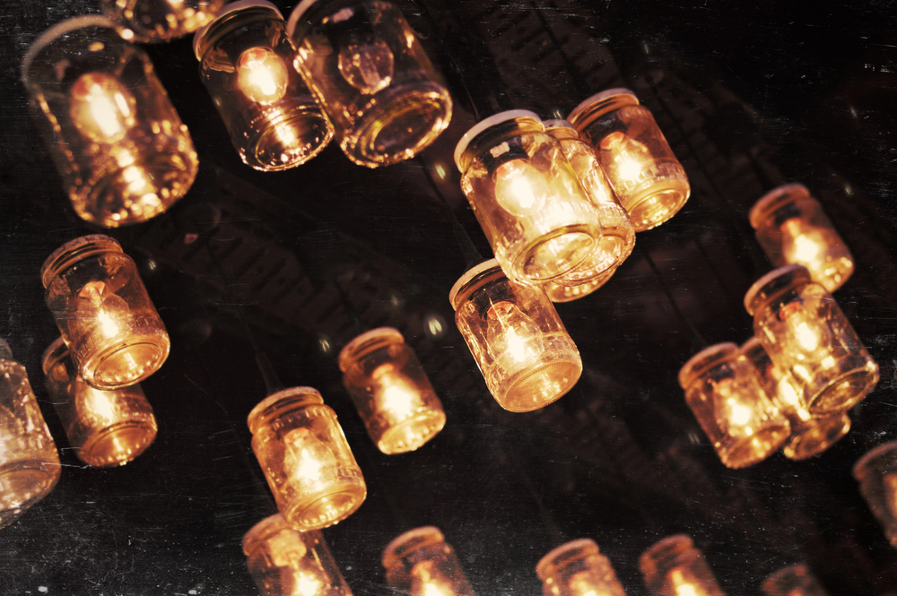 Mason jars filled with glowing light bulbs hang upside down from the ceiling, creating a warm, vintage ambience against a dark background.