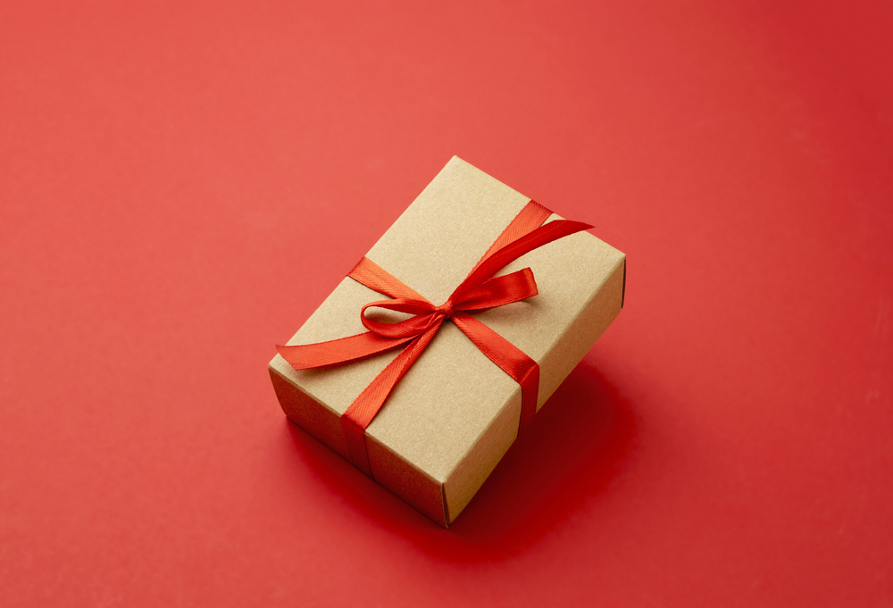 A small brown gift box tied with a red ribbon and bow, placed on a solid red background.