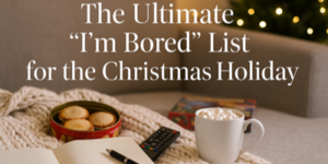 A cosy holiday scene with an open notebook, pen, tin of biscuits, TV remote, and a mug of hot chocolate on a blanket; text reads “The Ultimate ‘I’m Bored’ List for the Christmas Holiday.”.