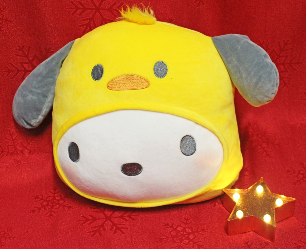 A soft toy resembling a character with a white face, grey ears, and a yellow hood with a beak, sits on a red background with snowflake patterns. A lit, star-shaped ornament is next to it.