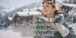 A smiling woman in ski gear holds skis over her shoulder with snowy chalets in the background. Text reads: From Chalet to Check-In: What First-Time Skiers Need to Know Before Booking.