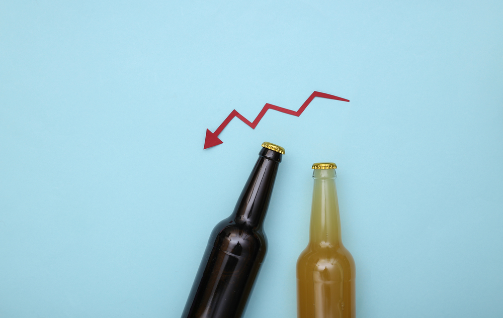 Two capped beer bottles on a blue background with a red zigzag arrow pointing downwards above them, symbolising a decline.