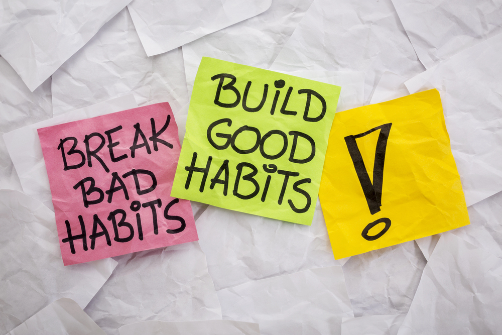 Three colourful sticky notes on crumpled white paper: one pink note reads BREAK BAD HABITS, a green note says BUILD GOOD HABITS, and a yellow note has a large exclamation mark.