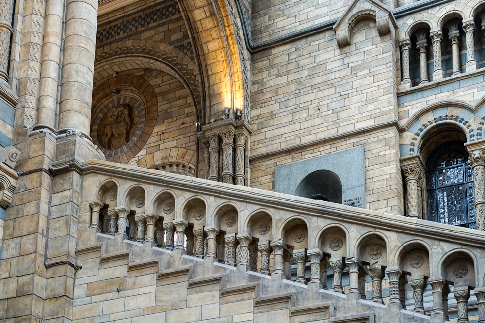 Stone staircase with ornate balustrades and columns inside a grand building with arched details, intricate carvings, and a decorative circular relief on the upper wall.