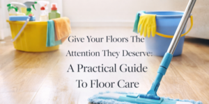 A blue mop cleaning a wooden floor with cleaning supplies and buckets in the background. Text reads: “Give Your Floors The Attention They Deserve: A Practical Guide To Floor Care.”.