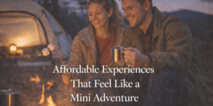 A smiling couple sits by a campfire roasting marshmallows, holding metal mugs, with a lit tent and camping gear in the background. Text reads: Affordable Experiences That Feel Like a Mini Adventure.