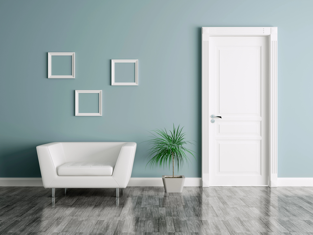 Minimalist room with a white armchair, three empty square frames on a blue wall, a potted plant, and a closed white door on a grey wood floor.