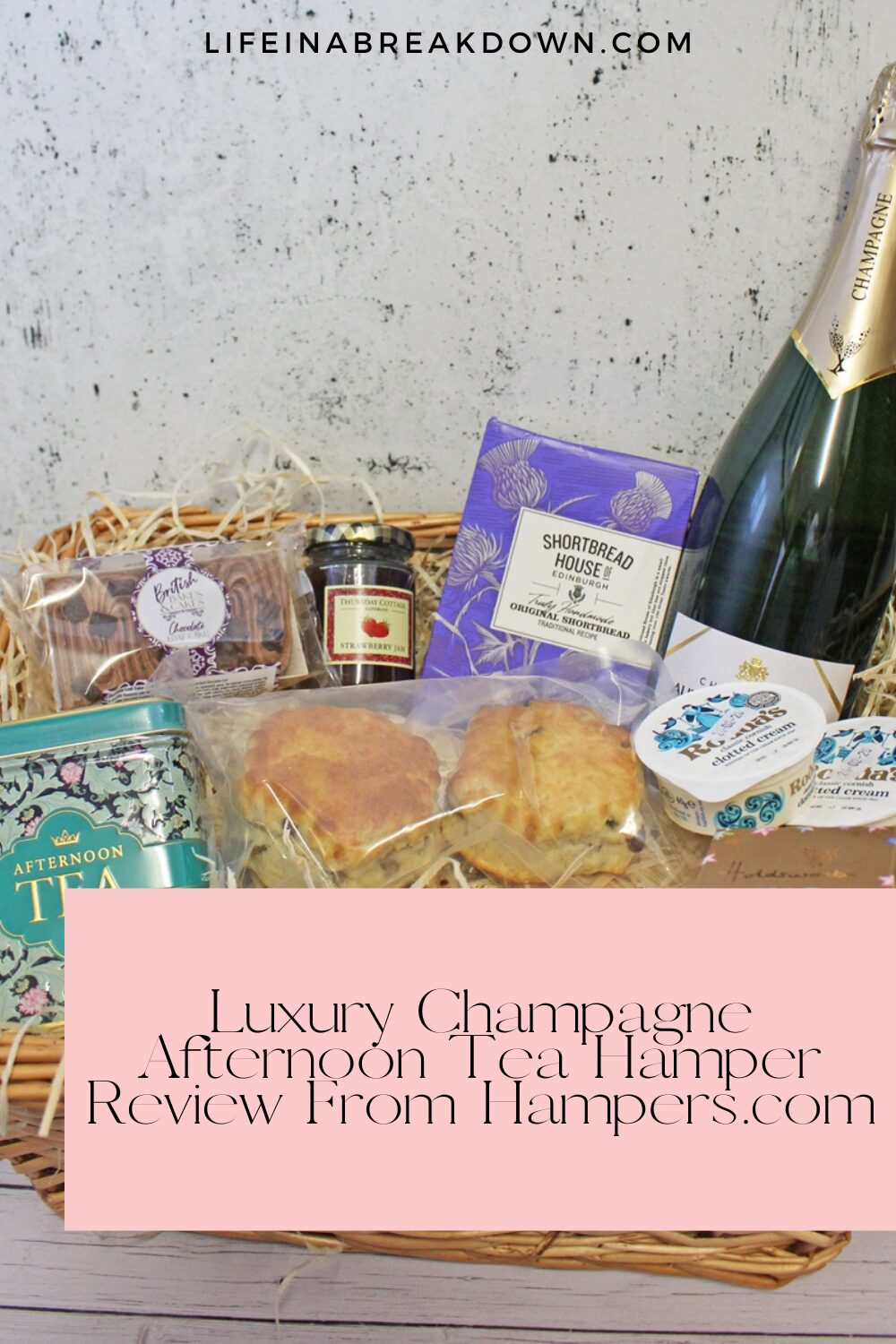 A wicker basket filled with luxury afternoon tea items, including a bottle of champagne, tea, shortbread, scones, jam, and clotted cream. Pink text overlay reads: “Luxury Champagne Afternoon Tea Hamper Review From Hampers.com”.