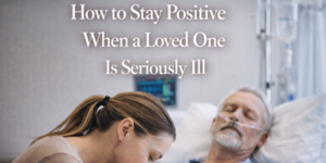 A woman rests her head on the bed of an older man with an oxygen tube, lying in a hospital bed. Text reads: How to Stay Positive When a Loved One Is Seriously Ill.