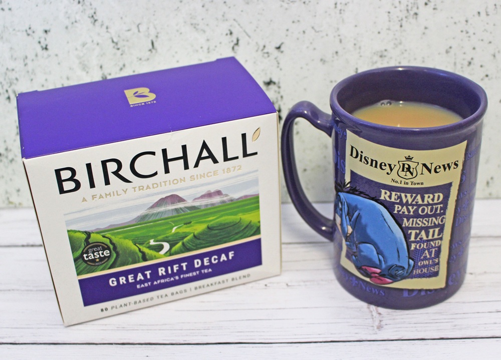 A box of Birchall Great Rift Decaf tea sits next to a Disney News mug filled with tea. The mug features Eeyore and text about a missing tail. Both items, popular for repeat purchases, rest on a white surface with a light background.