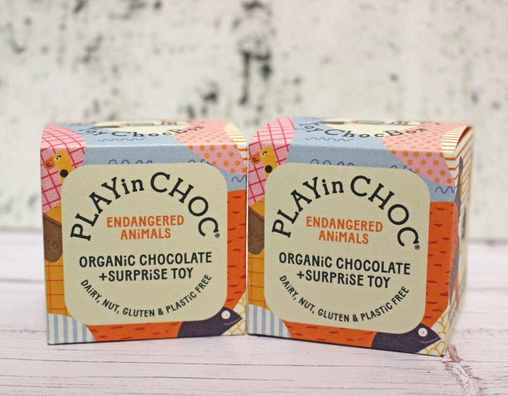 Two colourful boxes of PLAYin CHOC Endangered Animals Organic Chocolate + Surprise Toy sit side by side. The packaging highlights that the product is dairy, nut, gluten, and plastic free.