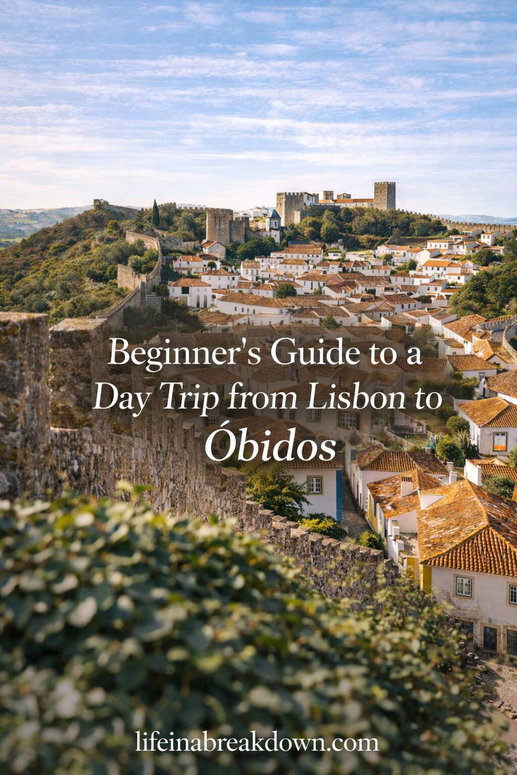 A scenic view of the medieval town of Óbidos, Portugal, with stone walls, white houses with orange roofs, and a castle in the background. Overlaid text reads: Beginners’ Guide to a Day Trip from Lisbon to Óbidos.