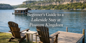 Two wooden chairs on a jetty overlook a calm lake with a floating boathouse and tree-covered cliffs in the background. Text reads: Beginner’s Guide to a Lakeside Stay at Possum Kingdom.