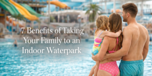 A family of three in swimsuits stands by an indoor waterpark pool, looking at the attractions. Text reads: 7 Benefits of Taking Your Family to an Indoor Waterpark.