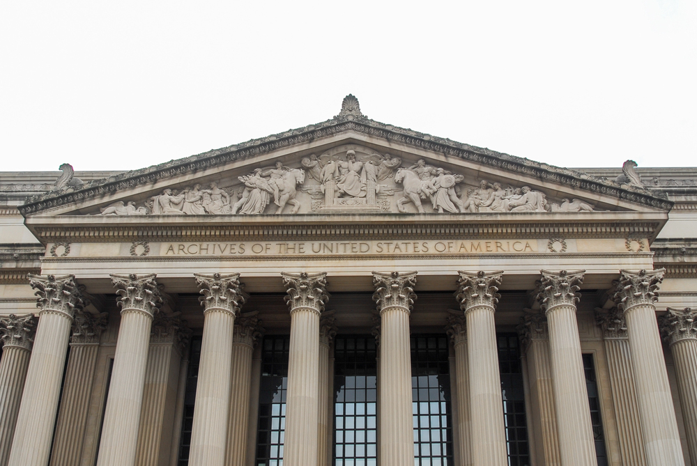 The facade of the National Archives building in Washington, D.C., featuring tall columns and a carved frieze above the entrance with the words Archives of the United States of America.