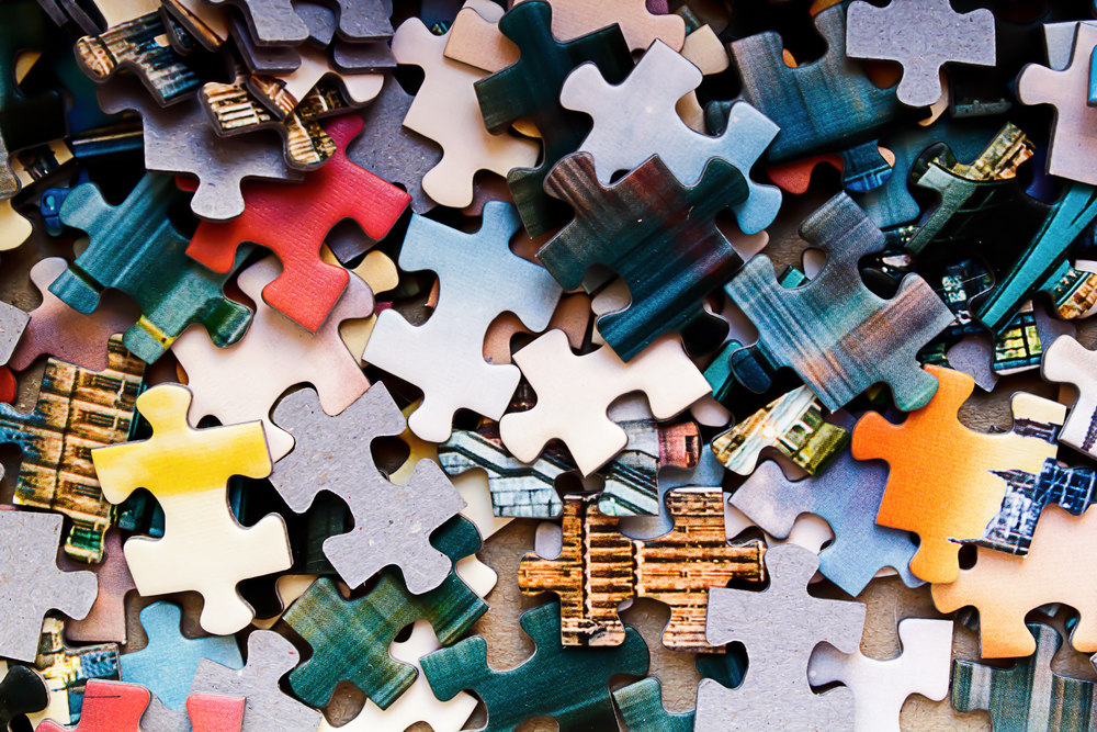 A close-up view of many colourful jigsaw puzzle pieces scattered randomly, showing various colours and patterns, but not forming a complete image.