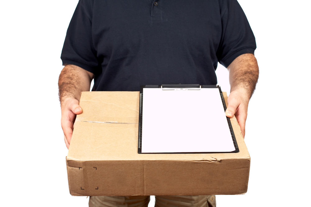 A person in a navy blue polo shirt holds a cardboard box and a clipboard with a blank sheet of paper against a white background.