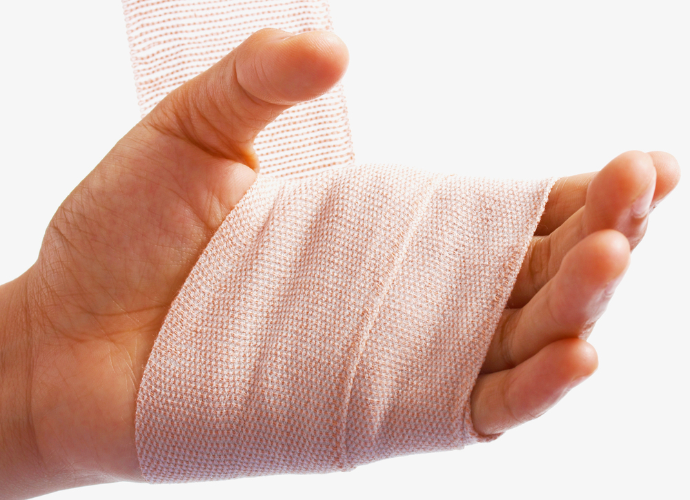 A close-up of a hand being wrapped with a beige elastic bandage, providing support or protection, against a plain white background.