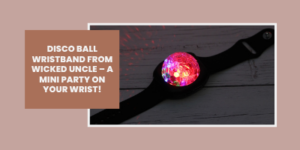 A black wristband with a colourful, glowing disco ball light in the centre sits on a wooden surface. Text on the left reads: Disco ball wristband from Wicked Uncle – a mini party on your wrist!.