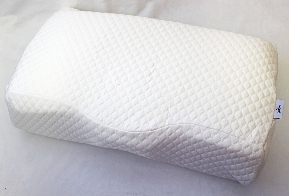 A white memory foam pillow with a textured, quilted cover and a contoured shape, placed on a plain light surface.