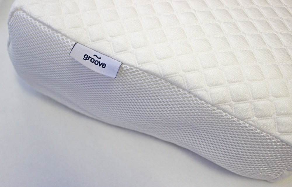 A close-up of a white pillow with a textured, quilted surface and a label that reads groove stitched onto the side. The pillow appears to have a mesh-like material along the edge.
