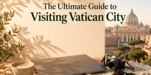 A laptop, coffee cup, and camera on a table overlook St. Peter’s Basilica under sunny skies, with text: The Ultimate Guide to Visiting Vatican City.