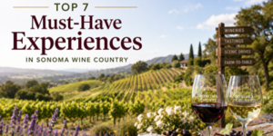 Two glasses of wine on a table overlook a scenic vineyard landscape in Sonoma Wine Country, with a wooden sign pointing to wineries, tastings, scenic drives, and farm-to-fork experiences. Text reads Top 7 Must-Have Experiences.