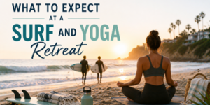 A woman sits cross-legged on the beach at sunset, facing the sea. Two people with surfboards walk towards the water. The text reads: What to Expect at a Surf and Yoga Retreat. Towels and water bottles are nearby.
