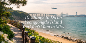A scenic coastal walking path with flowers and trees beside a sandy beach, a bridge over the water, an aeroplane flying above, and text that reads 10 Things to Do on Yeongjongdo Island You Won't Want to Miss.