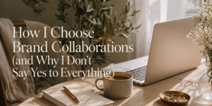 A cosy workspace with a laptop, coffee mug, notebook, pen, and small vase of flowers on a wooden table, with sunlight streaming in and text overlay about choosing brand collaborations.