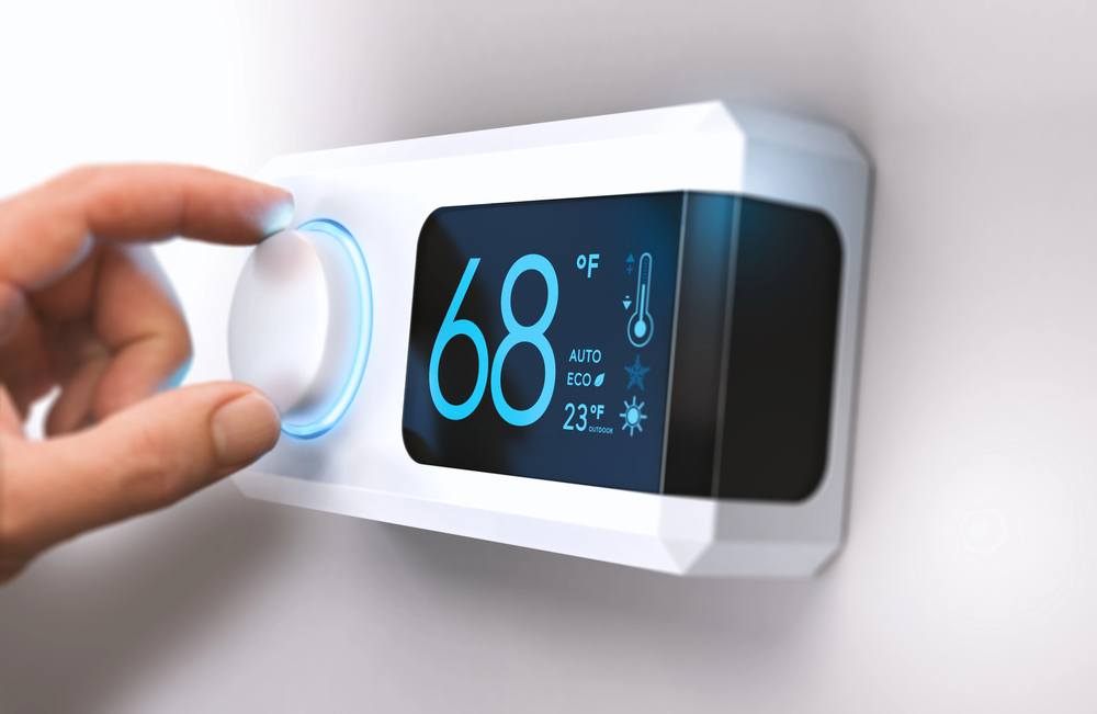 A hand is adjusting a smart thermostat mounted on a wall. The digital display shows the temperature set to 68°F, along with other settings like auto, eco, and the current indoor temperature of 23°C.