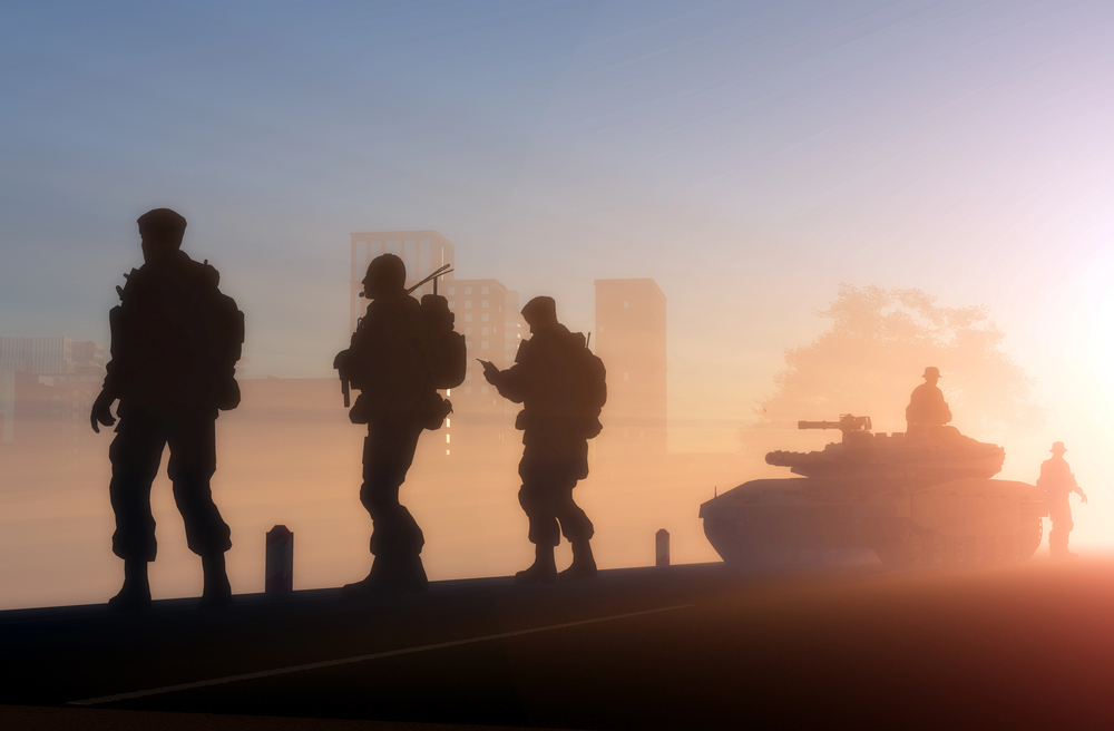 Silhouettes of four soldiers walking near a tank at sunrise or sunset, with a city skyline and trees visible in the misty background.
