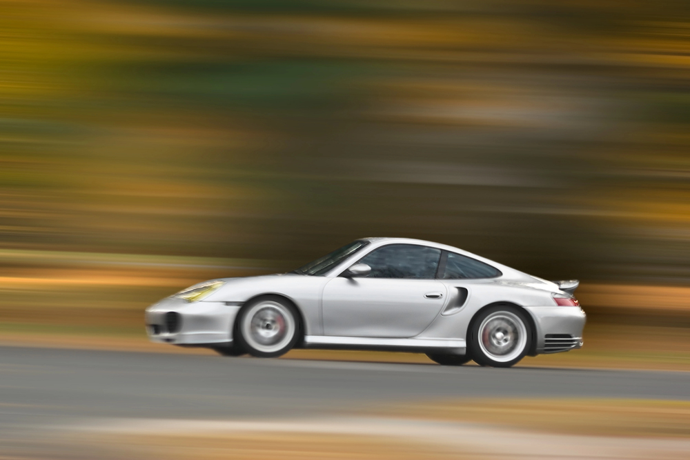 A silver sports car speeds down a road, with a blurred background of autumn colours emphasising its motion.