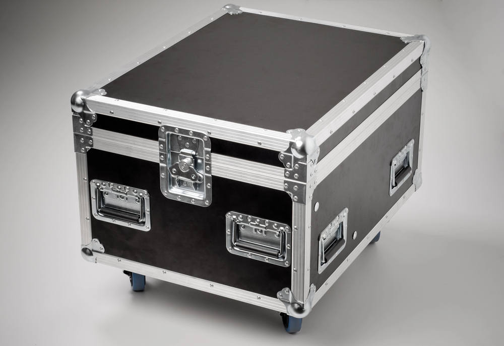 A large, black flight case with metal edges, reinforced corners, catches, and handles, designed for transporting equipment safely. The case is elevated on four small feet.