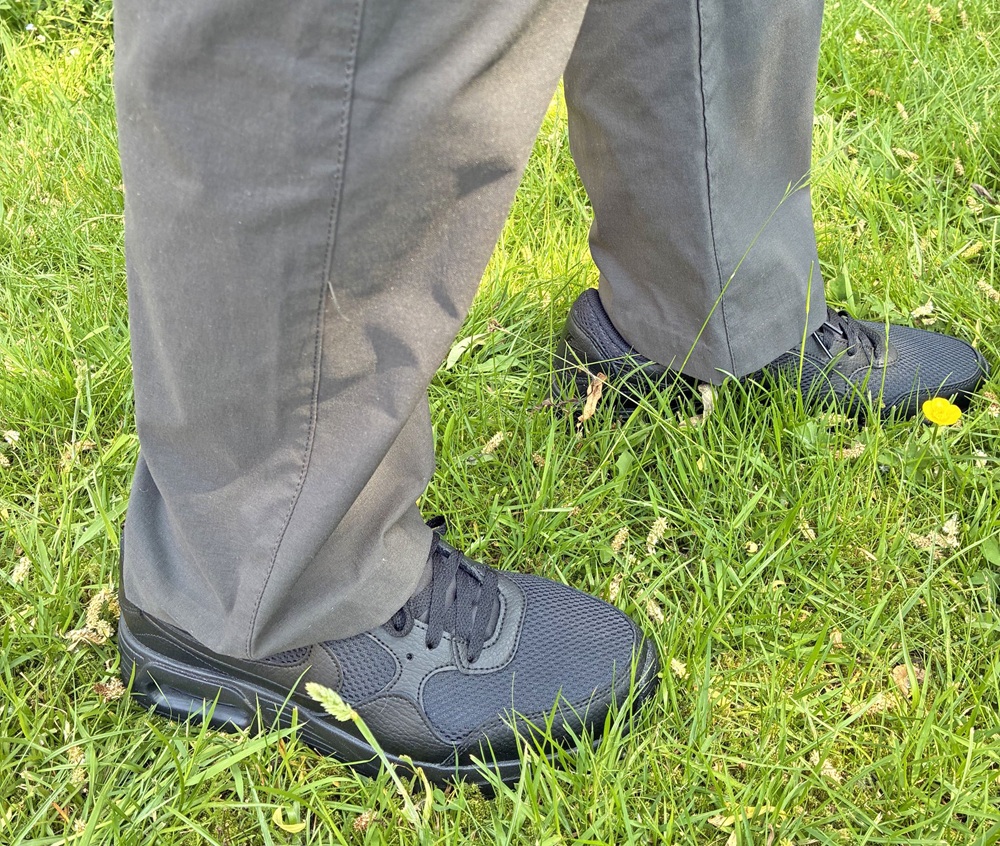 A person wearing dark grey trousers and black trainers is standing on green grass. Only the lower legs and feet are visible in the image—perfect inspiration for Father’s Day gift ideas focused on style and comfort.