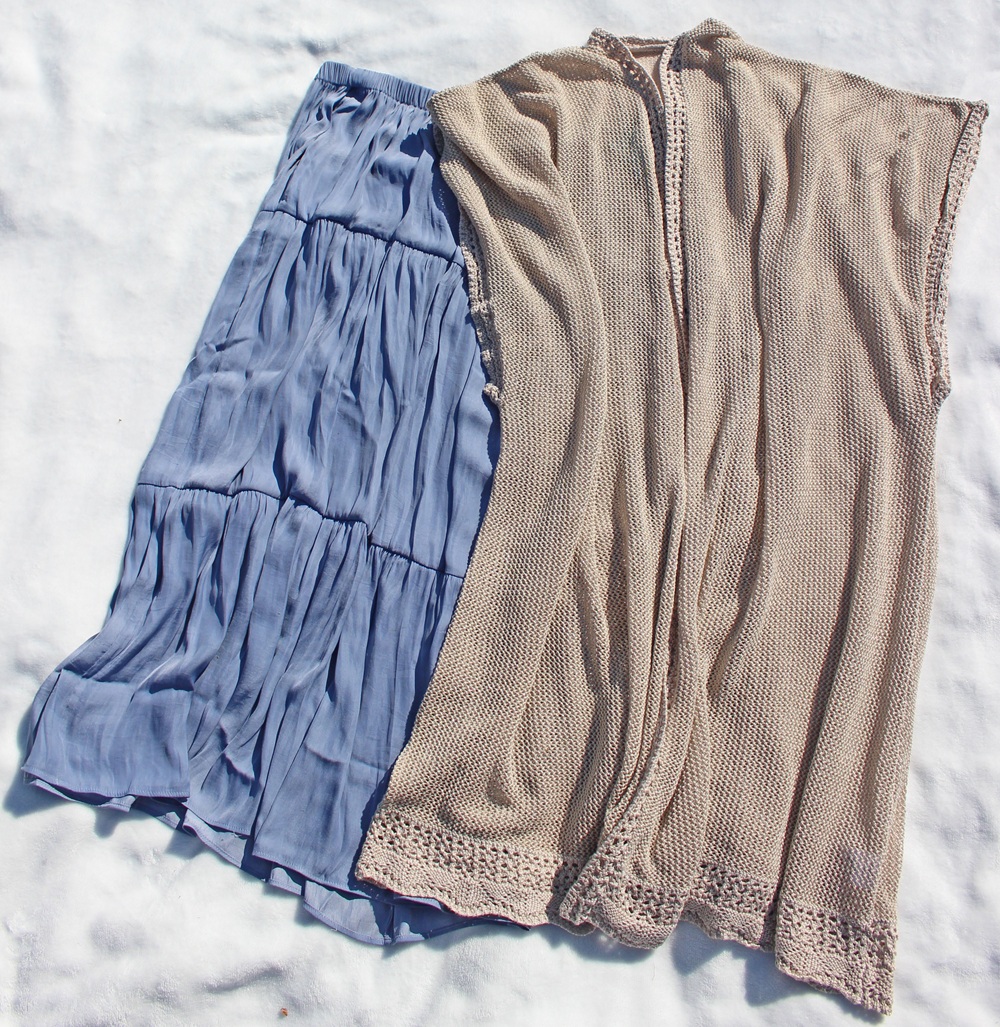 A light blue, tiered skirt and a beige, sleeveless knitted cardigan are laid out side by side on a white surface.