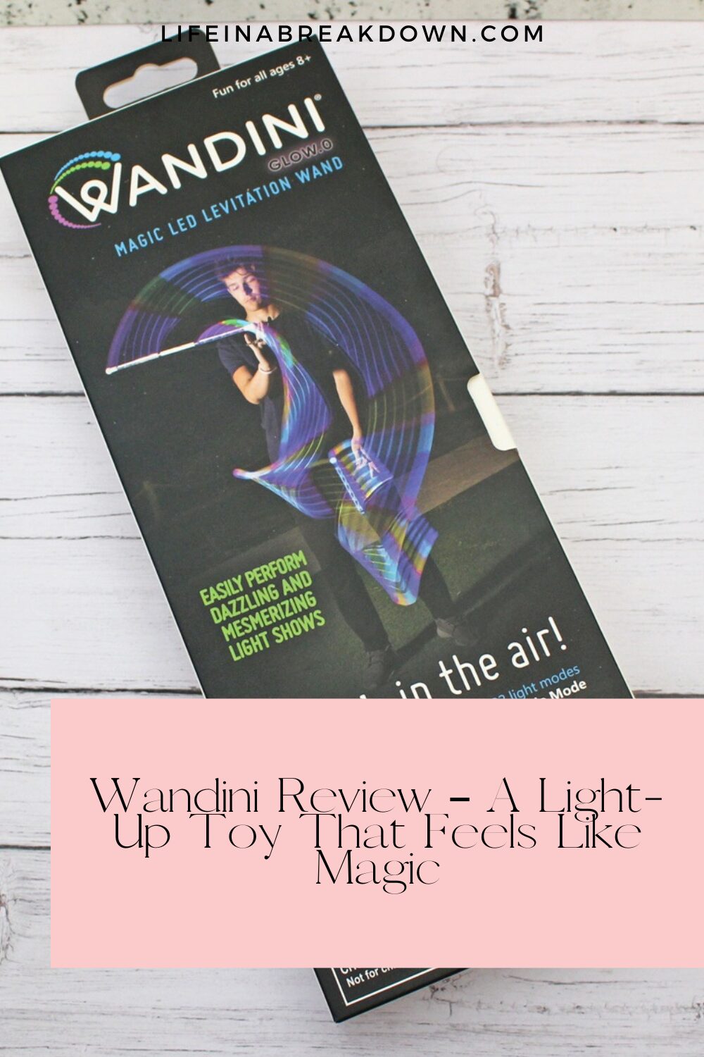 A box of the Wandini Magic LED Levitating Wand toy is displayed on a light wooden surface, showing a child waving a glowing, colourful wand with swirling light trails, and text describing its features.