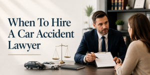 A solicitor in a suit discusses paperwork with a woman at a desk. Model cars and scales of justice sit on the desk. Text reads: When To Hire A Car Accident Solicitor.