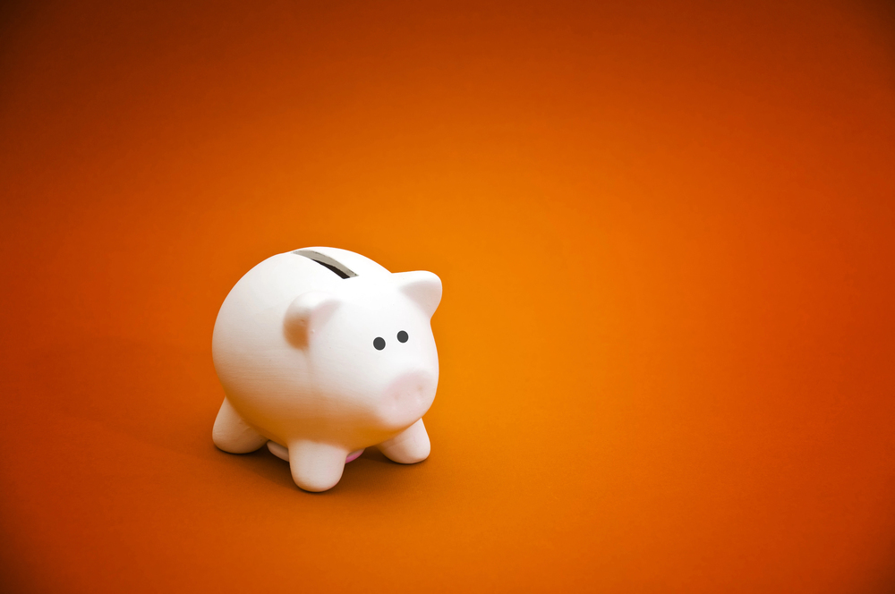 A white piggy bank with black eyes sits on an orange background, positioned slightly to the left in the frame.