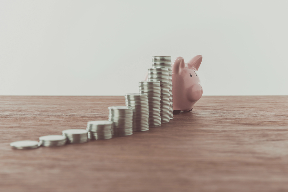 Stacks of coins arranged in ascending order leading to a pink piggy bank on a wooden surface, representing savings growth or financial planning.