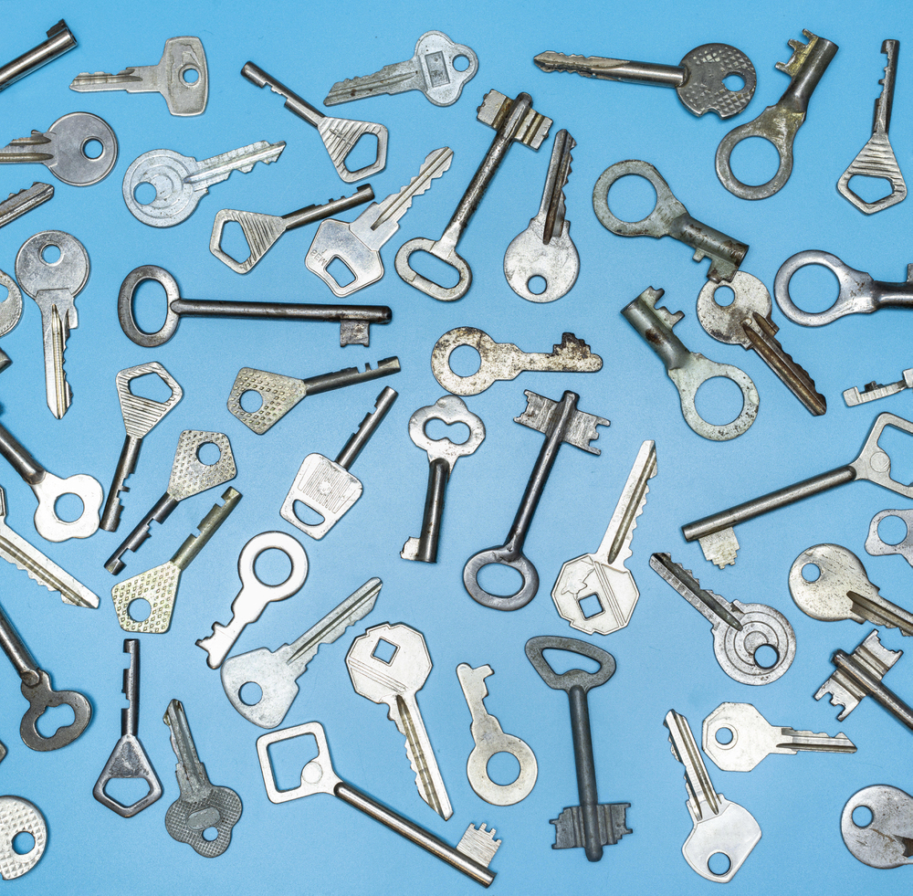Assorted old and modern metal keys scattered on a flat blue surface, featuring various shapes, sizes, and designs.