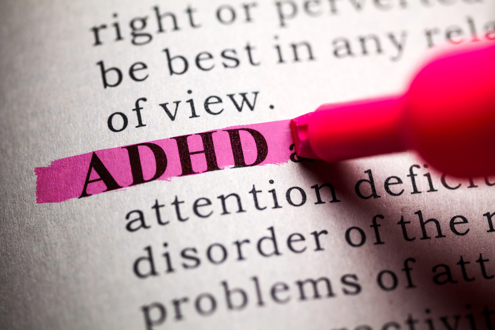 A pink highlighter marks the word ADHD on a printed page, emphasising the term in a larger block of text about attention deficit disorder.