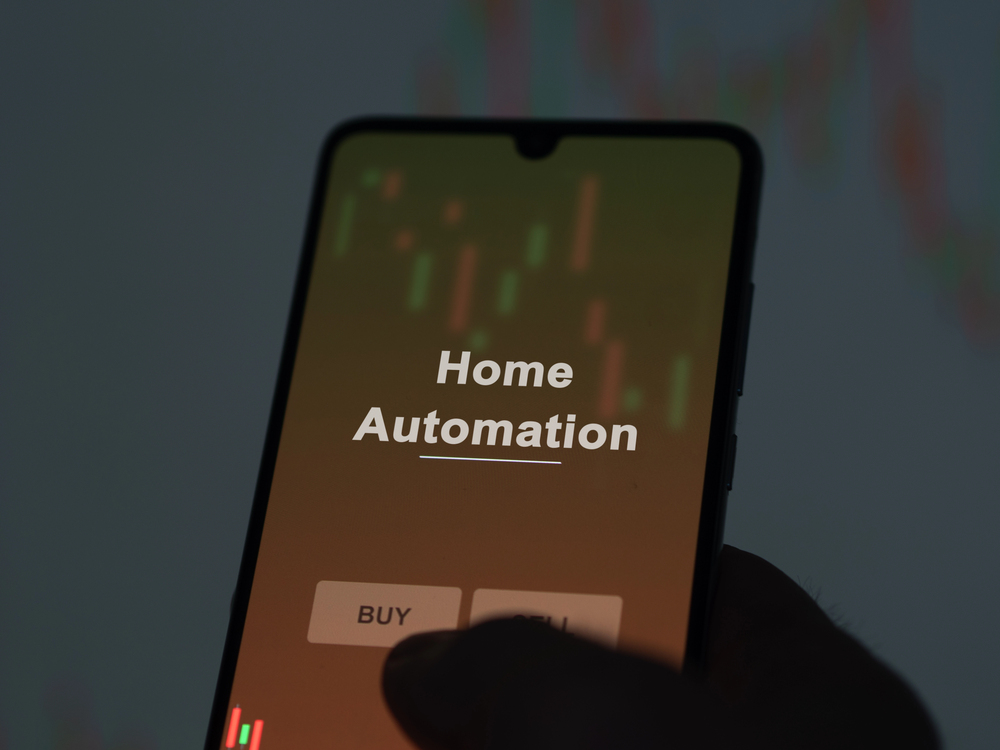 A smartphone screen displays the words Home Automation with BUY and another partially visible button below, held in a person's hand against a blurred background with coloured vertical lines.