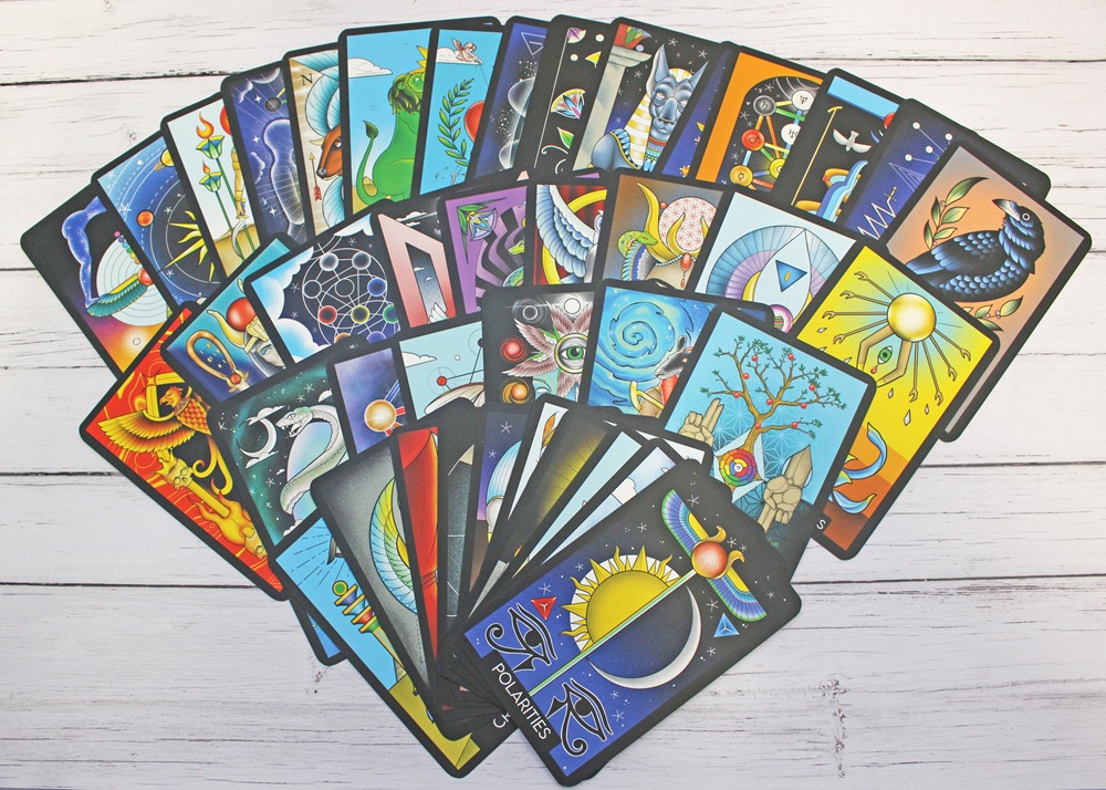 A colourful fan of tarot cards with vibrant, abstract illustrations featuring celestial, animal, and dreamlike designs is spread out on a white wooden surface.