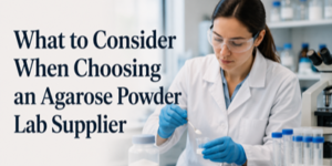 A female scientist in a lab coat and safety goggles measures powder in a laboratory. Text reads: What to Consider When Choosing an Agarose Powder Lab Supplier.