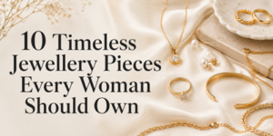 Gold rings, necklaces, a bracelet, and pearl earrings are arranged on cream fabric next to a ceramic dish. Text reads: 10 Timeless Jewellery Pieces Every Woman Should Own. Dried flowers are visible on the left.
