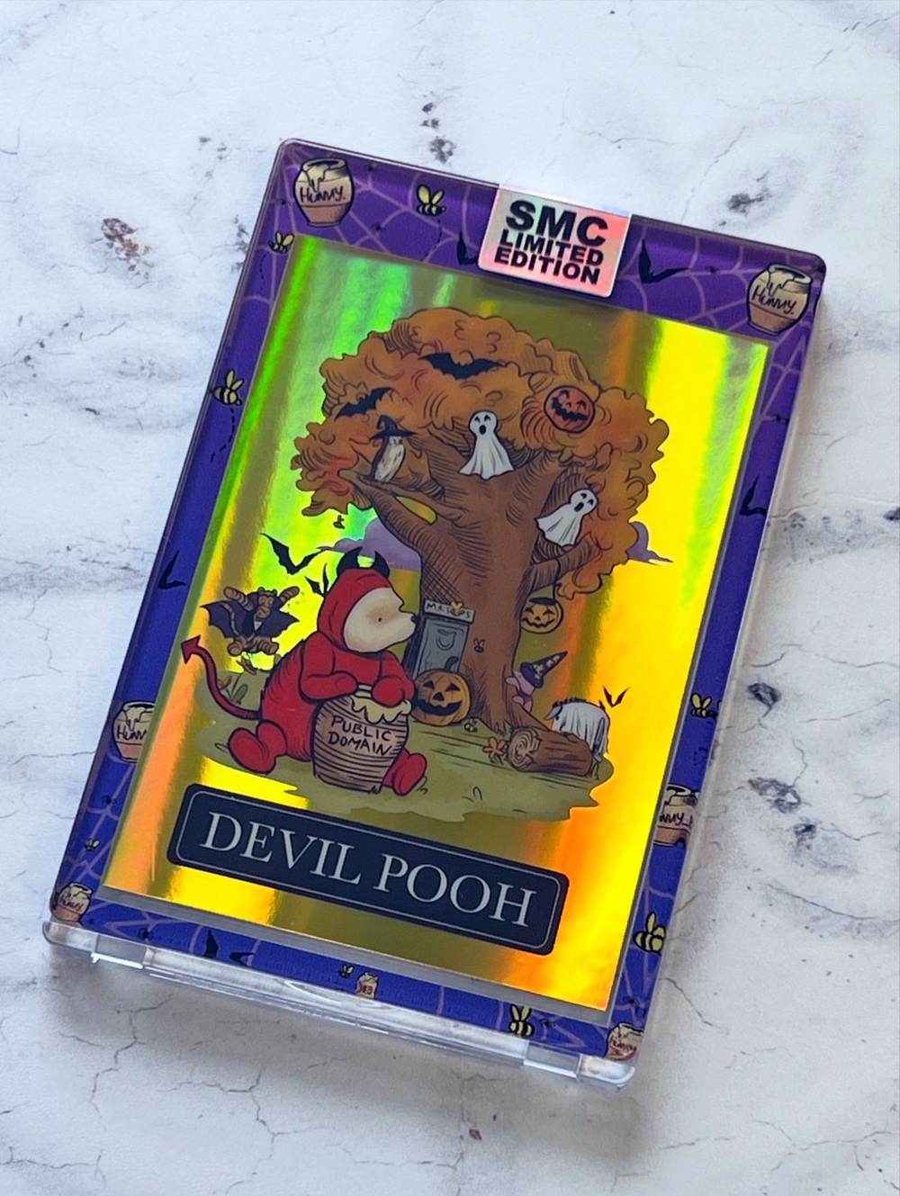 A holographic trading card shows Winnie the Pooh in a red devil costume near a spooky tree with ghosts, pumpkins, and bats. The card reads DEVIL POOH and has an SMC Limited Edition label.