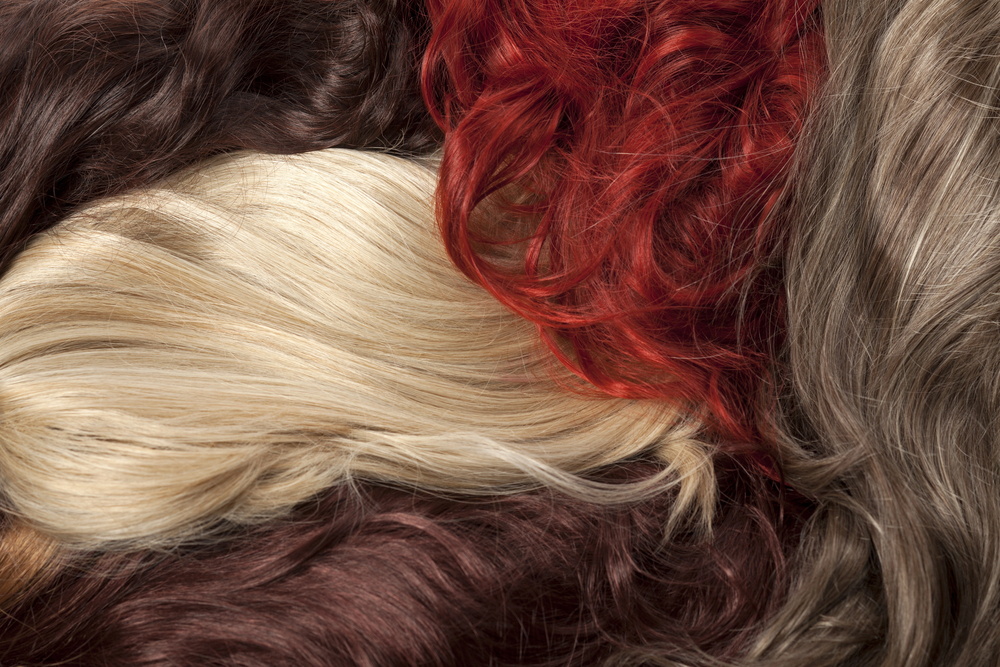 A close-up view of various coloured hair strands, including blonde, red, brown, and dark brown, arranged together in a textured, overlapping pattern.